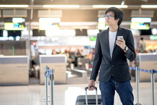 Young asian man with his suitcase luggage using smartphone while waiting for airline flight in the international airport terminal, business travel and online check in concepts