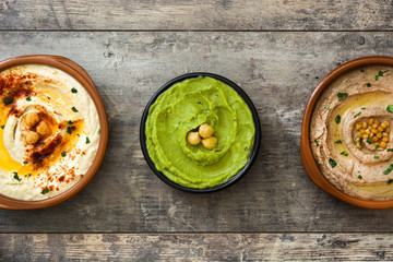 Different hummus bowls. Chickpea hummus, avocado hummus and lentils hummus on wooden table
