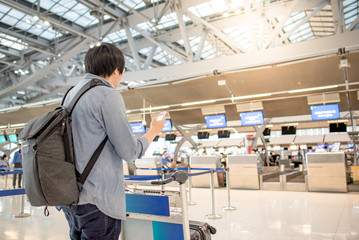 young asian check in online by using smartphone and waiting for drop his luggage at airline check-in counter inside the international airport terminal, travel lifestyle concept