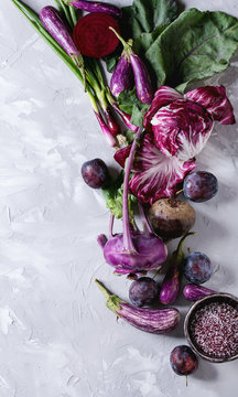Assortment raw organic of purple vegetables mini eggplants, spring onion, beetroot, radicchio salad, plums, kohlrabi, flower salt over gray concrete background. Top view with space