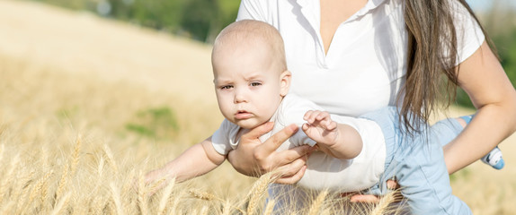 Portrait of a small newborn baby boy on his mother's arms in wheat field at sunny summer day