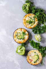 Baked homemade vegetable broccoli quiche pie in mini metal forms served with fresh greens on gray...