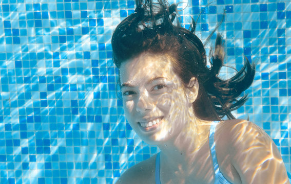 Girl swims in pool underwater, happy active teenager dives and has fun under water, kid fitness and sport on family vacation
