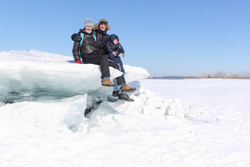 Fototapeta na wymiar Happy family sitting on an ice floe on a frozen river in winter, Ob River, Russia