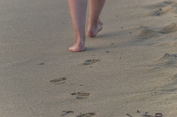 Spuren im Sand am Strand einer gehenden Frau mit Beinen im Anschnitt, nackte Haut