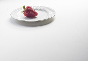 Isolated red strawberry on white plate on plain white background