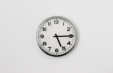 White Clock hanging on a white wall showing time 5:15