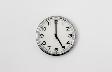 White Clock hanging on a white wall showing time 5:00