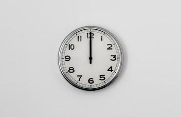 White Clock hanging on a white wall showing time 12:00 