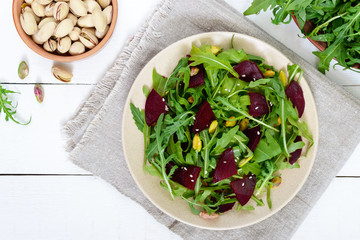 Spicy vegan salad of beets, arugula, pistachio nuts on a plate on a white background. Top view.