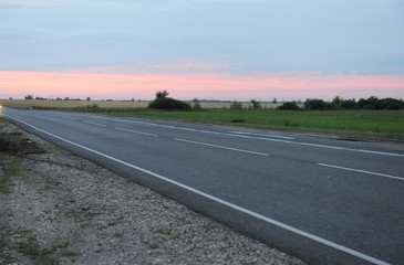 Pink sunset on an empty road with markings. Country landscape. Atmosphere of travel