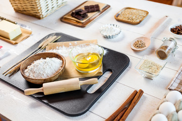 Baking ingredients in rural kitchen - dough recipe ingredients (eggs, flour, milk, butter, sugar) and rolling pin on wooden white table.