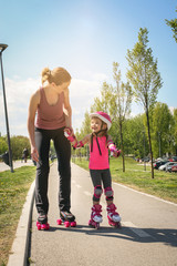 Mother and her little daughter inline skating on sidewalk. Mother and daughter enjoying in spring...