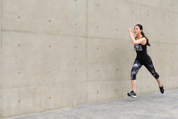 Fototapeta na wymiar smiling female runner running on gray wall