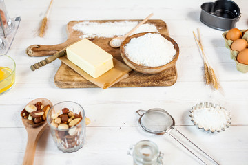 Baking ingredients in rural kitchen - dough recipe ingredients (eggs, flour, milk, butter, sugar) and rolling pin on wooden white table.