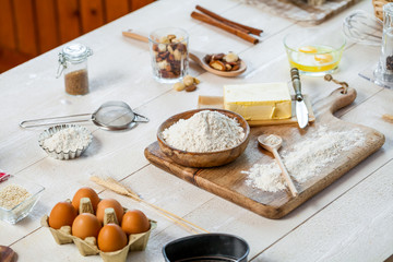Baking ingredients in rural kitchen - dough recipe ingredients (eggs, flour, milk, butter, sugar) and rolling pin on wooden white table.
