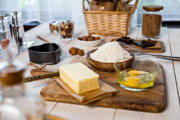 Baking ingredients in rural kitchen - dough recipe ingredients (eggs, flour, milk, butter, sugar) and rolling pin on wooden white table.