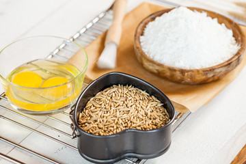 Baking ingredients in rural kitchen - dough recipe ingredients (eggs, flour, milk, butter, sugar) and rolling pin on wooden white table. Close up