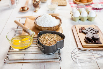 Baking ingredients in rural kitchen - dough recipe ingredients (eggs, flour, milk, butter, sugar) and rolling pin on wooden white table. Close up