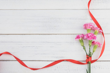 Pink carnation flowers bouquet with red ribbon on white wood background with copy space