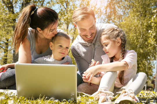 Happy family using laptop, sitting on the green grass. Family enjoying on the meadow in the spring day.
