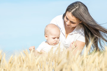 Happy young family of a beautiful mother and small newborn baby in wheat field at sunny summer day. Blue sky background for copyspace