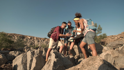 Young people with backpacks on rocky coastline exploring man together trying to find way.