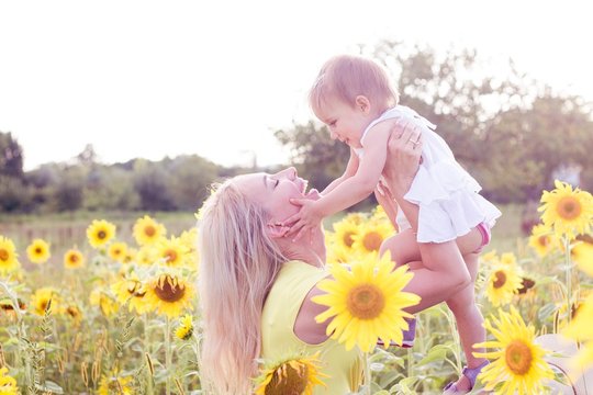 Family is walking along the summer flowering field. Happy mother and daughter in the sun. Summer. Sunflowers.