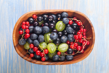 Red black currant blueberry gooseberry in a wooden bowl