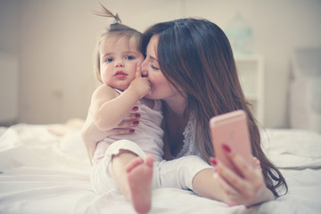 Mother with her little baby having fun in the bed. Mother making self-picture with her cute little baby in the bed.