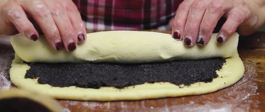 Process of making strudel pie, woman's hands wrapping the dough with poppy stuffing on wooden board.