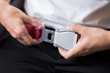 Close up of passenger hands fasten belts while sitting on airplane seat.