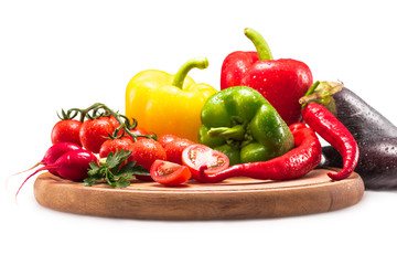 cherry tomatoes, different peppers and radish on wooden cutting board, isolated on white