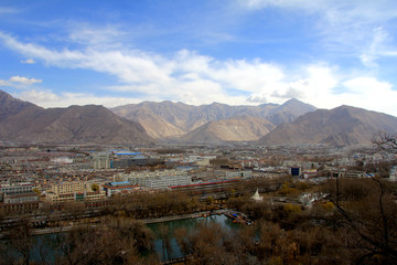 The panoramic view of Lhasa city, in front of  Potala Palace and Palace square, with modern building and mountains, far away a Tibet Peaceful Liberation Monument and blue sky
