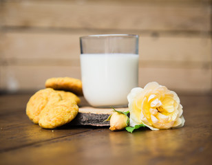 carrot cookies, glass of milk on the old wooden background with rose flower