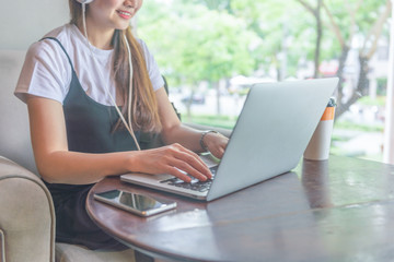 Young woman sitting beside window, wearing headphone and using laptop