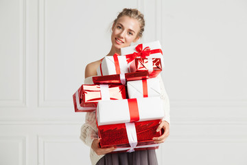 Happy girl with a bunch of presents red and white smiling standing in white interior