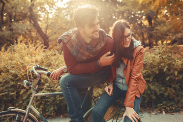 Young couple riding bicycle outdoors at autumn day.They sitting on bike and making fun.