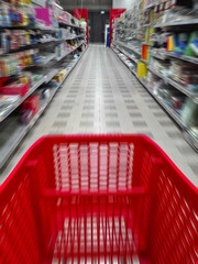 blurred image of a cart trolley in a supermarket aisle with shelves on both sides.