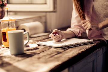 Young girl writing in notebook in the kitchen. Home interior, female having breakfast writing on wooden desk. Toned image.