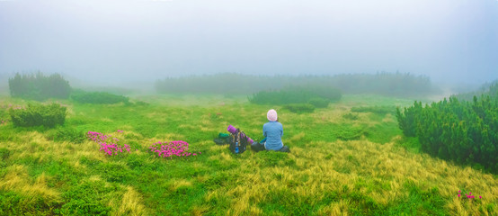 Woman tourist resting on a mountain meadow among the flowers in the fog