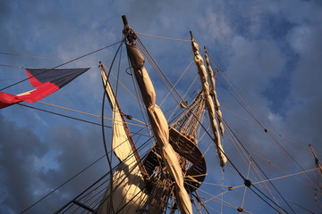 Tall ship masts and rigging silhouetted against a dramatic sky at sunset