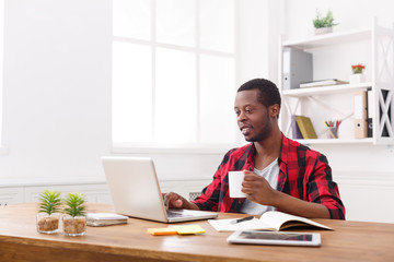 Relaxed black businessman in casual office, work with laptop, drink coffee