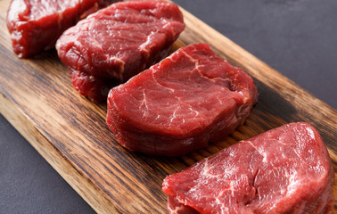 Raw beef filet mignon steaks on wooden board at gray background