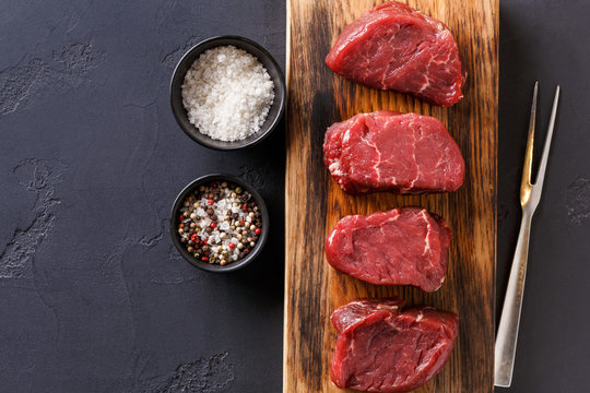Raw beef filet mignon steaks with spices on wooden board at black background