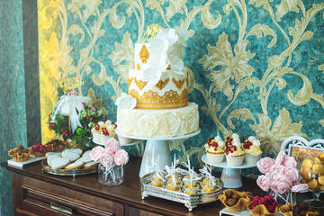Luxury wedding candy bar with a beautiful white cake decorated with gold ornaments. Concept of chic wedding desserts