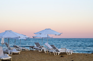 Sanset on sea with golden sand and straw-colored umbrellas.
