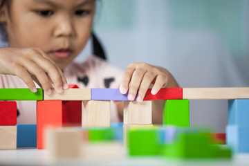 Focus on hands of cute little child girl  playing with colorful wooden blocks in the room