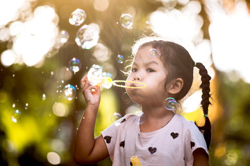 Cute asian child girl having fun to blow soap bubbles in outdoor at sunset
