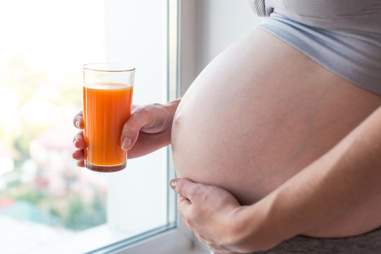 Pregnant woman with belly holding a glass of carrot juice in hand. Concept for weight control and healthy eating